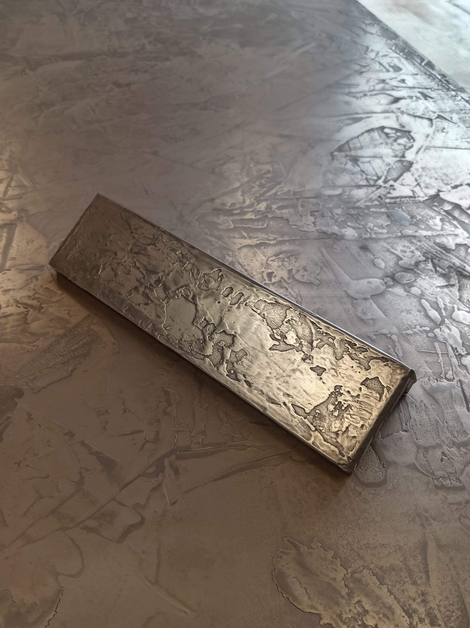 Hand-textured liquid metal panel sample resting on a larger liquid-metal surface
