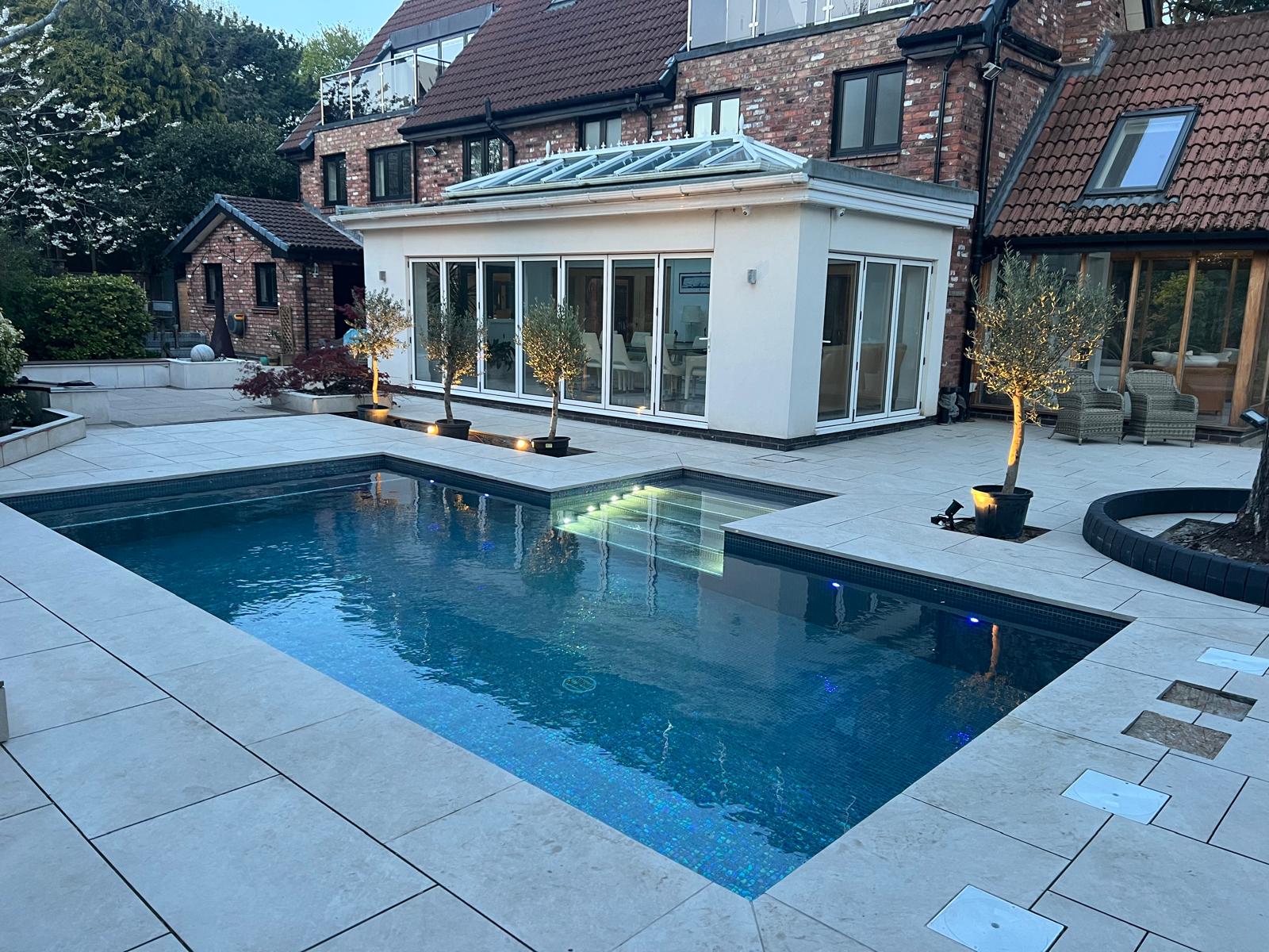 Stone pool coping with a bullnosed edge around an outdoor pool and patio at dusk
