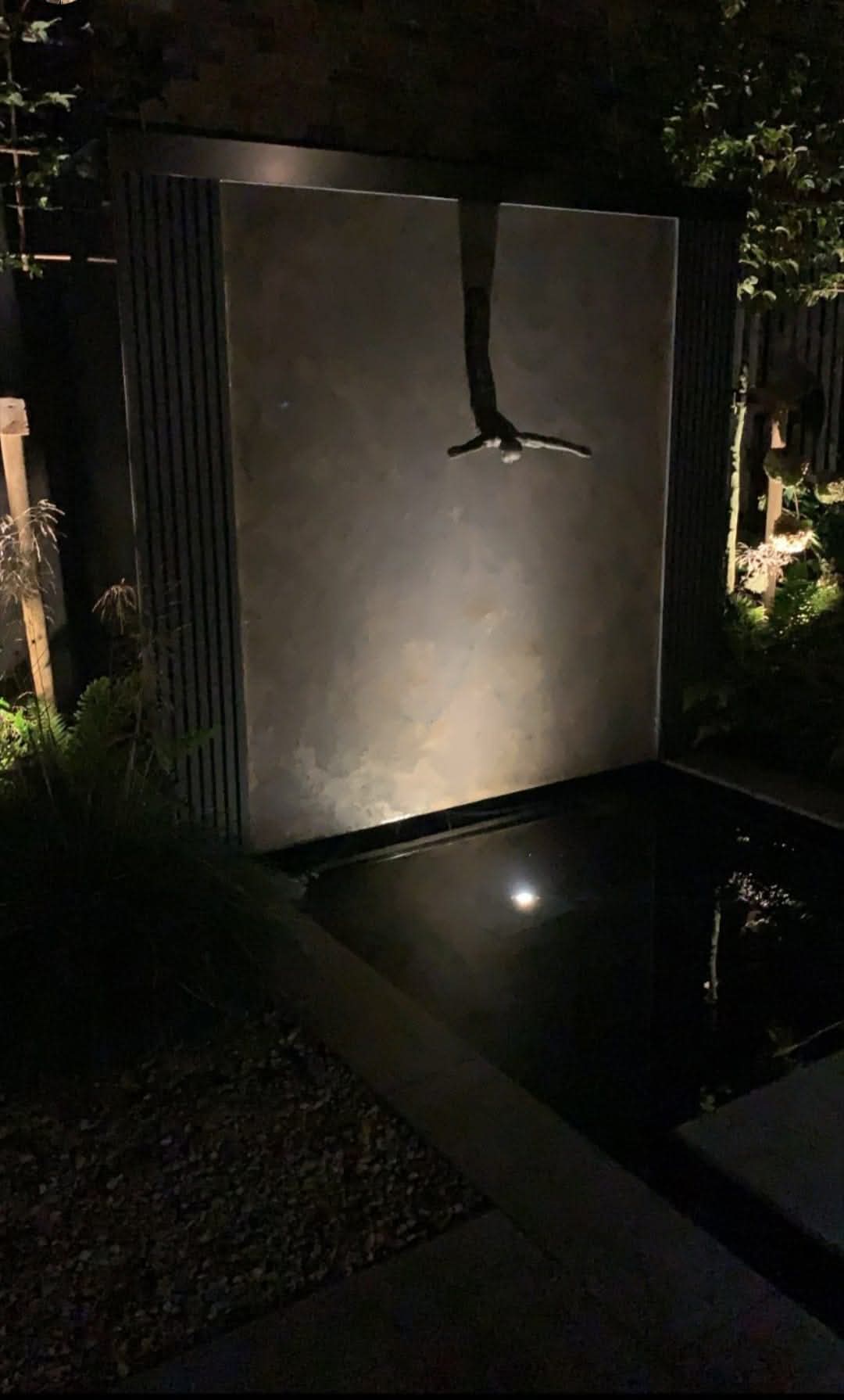 One-off bespoke natural stone water feature wall beside a pond at night