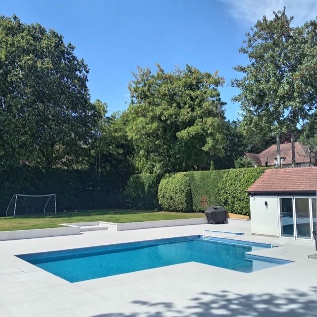 Completed swimming pool with light stone paving in a garden