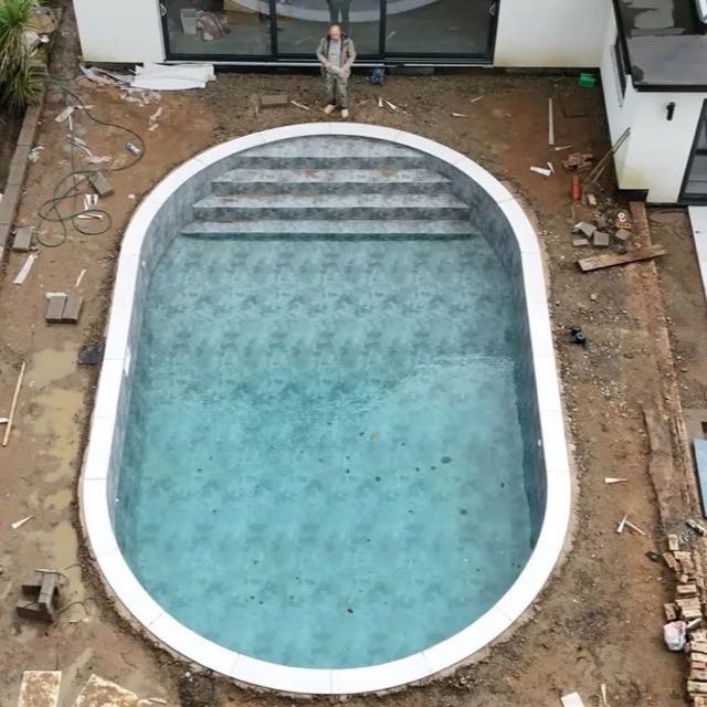 Aerial view of a curved porcelain pool with a full bullnose stone coping