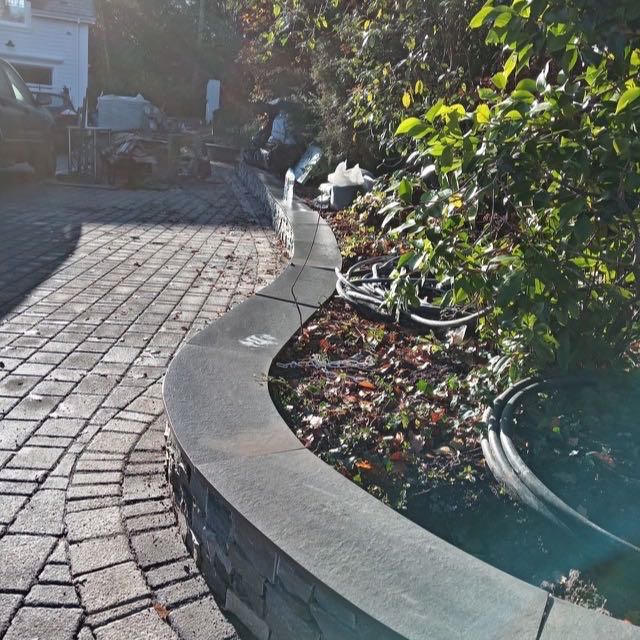 Curved stone-capped raised bed beside a driveway