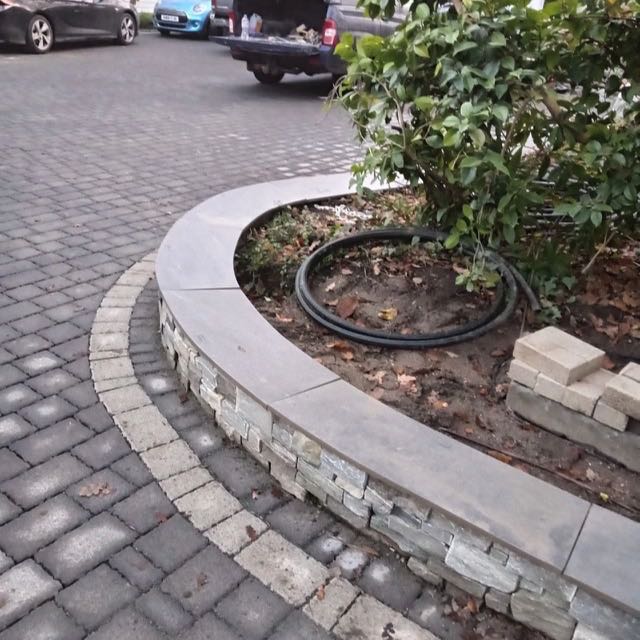 Curved stone coping on a retaining wall beside a driveway