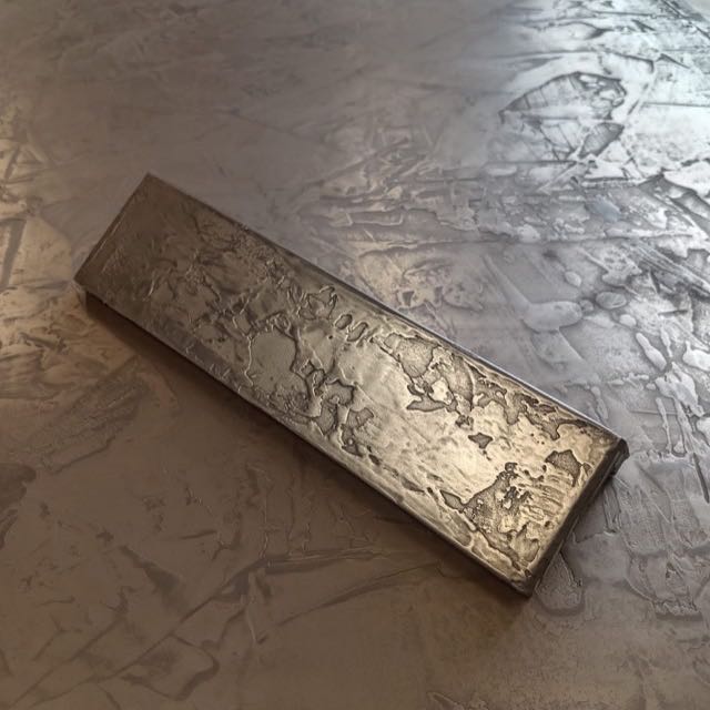 Hand-textured liquid metal panel sample resting on a larger liquid-metal surface