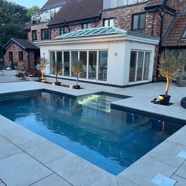 Outdoor pool with stone coping and patio photographed at dusk
