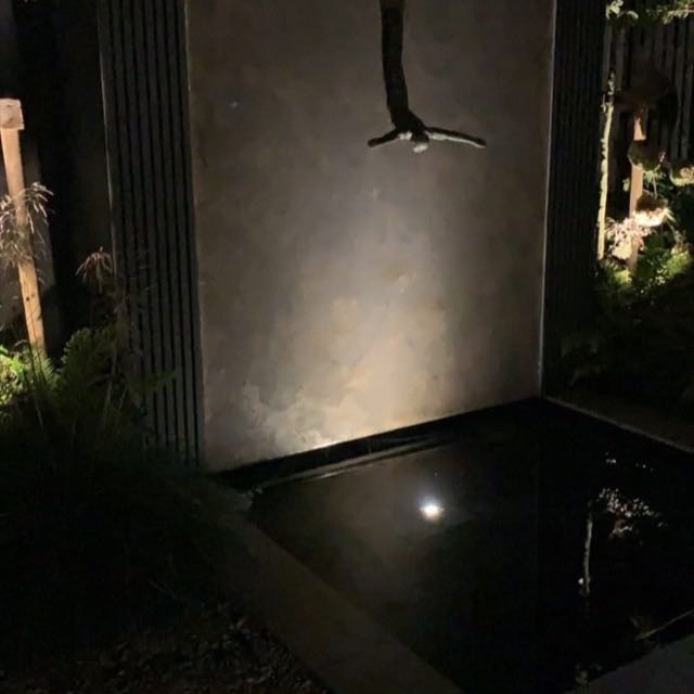 Stone water feature wall beside a pond at night