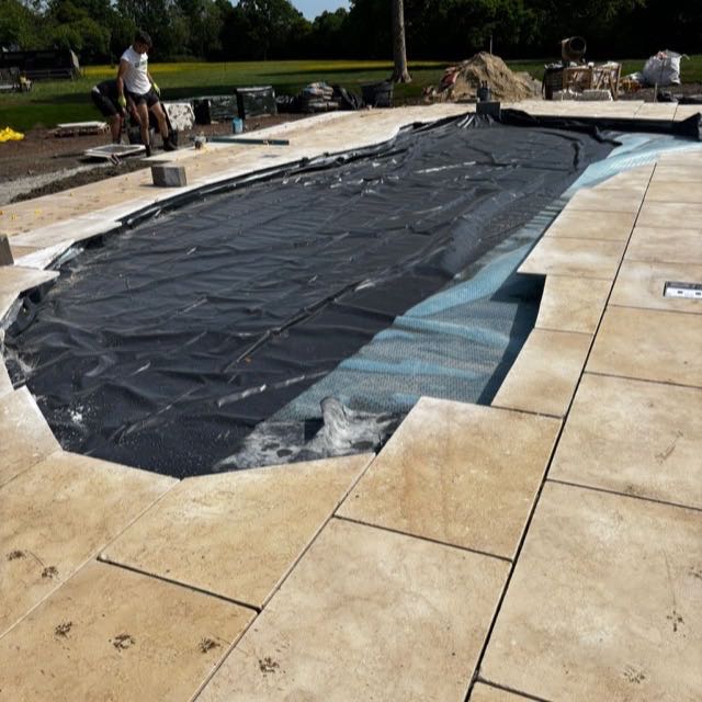 Stone paving being installed around a swimming pool under construction